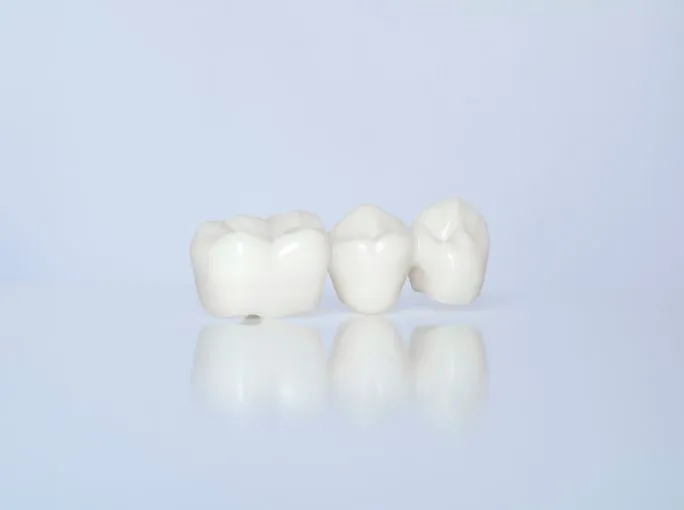 Three white ceramic dental crowns on a pale blue background